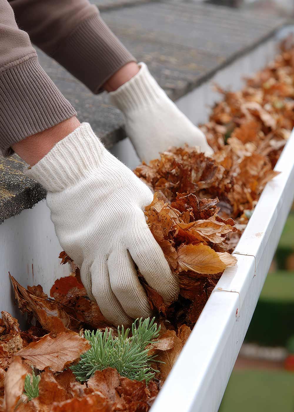 Empire Gutter Cleaning technician clearing leaves from gutters at a Rochester, NY home.